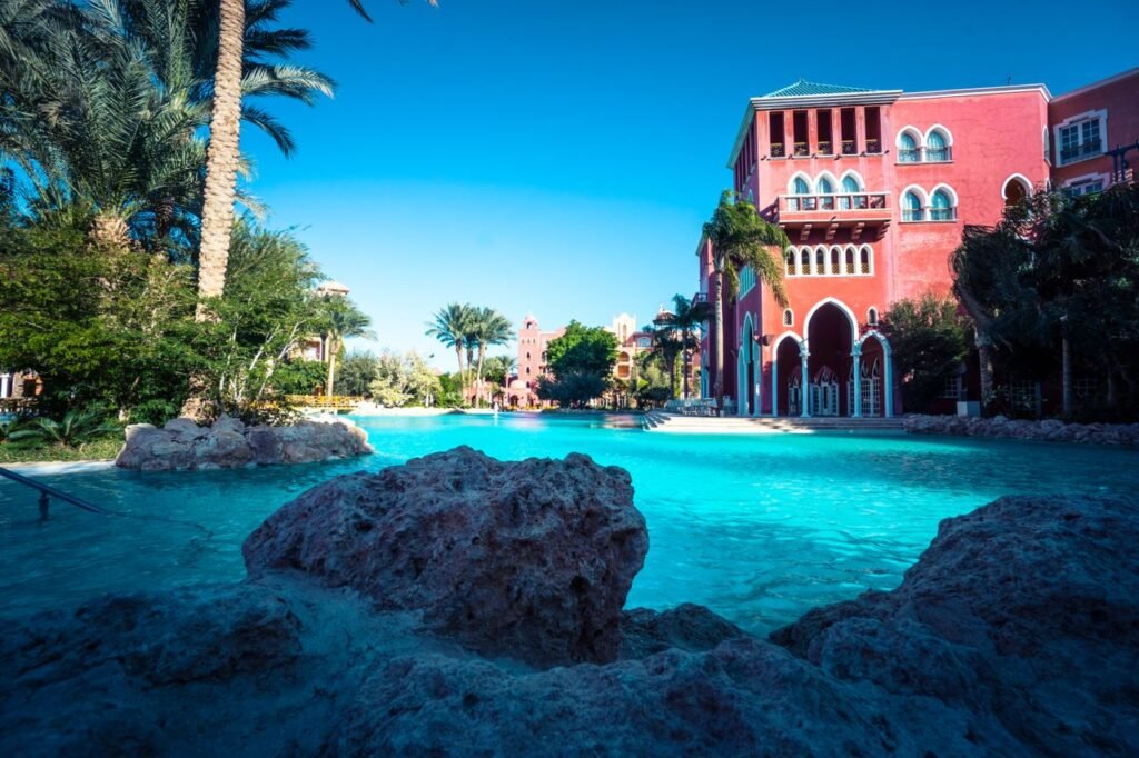 Stunning resort poolside area with palm trees and vibrant red architecture on a sunny day.
