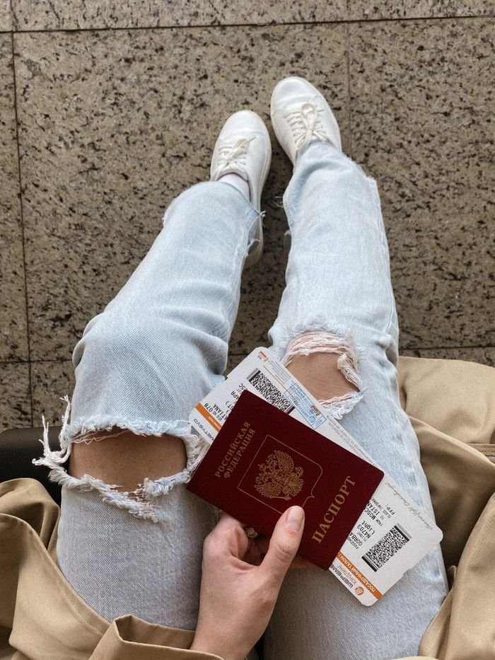 High-angle view of a person holding a passport and boarding passes, wearing ripped jeans and sneakers.